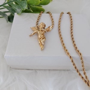 May include: A gold chain necklace with a small angel pendant. The chain is a rope style and the pendant is detailed with wings and a halo.