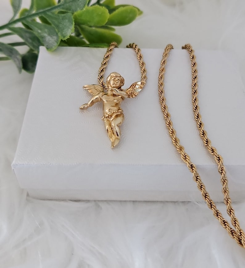 May include: A gold chain necklace with a small angel pendant. The chain is a rope style and the pendant is detailed with wings and a halo.