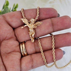 May include: Gold chain necklace with a gold cherub pendant. The chain is a rope style and the pendant is detailed.