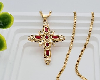 May include: A gold chain necklace with a red and white cross pendant. The cross is decorated with small white stones and red oval-shaped stones.