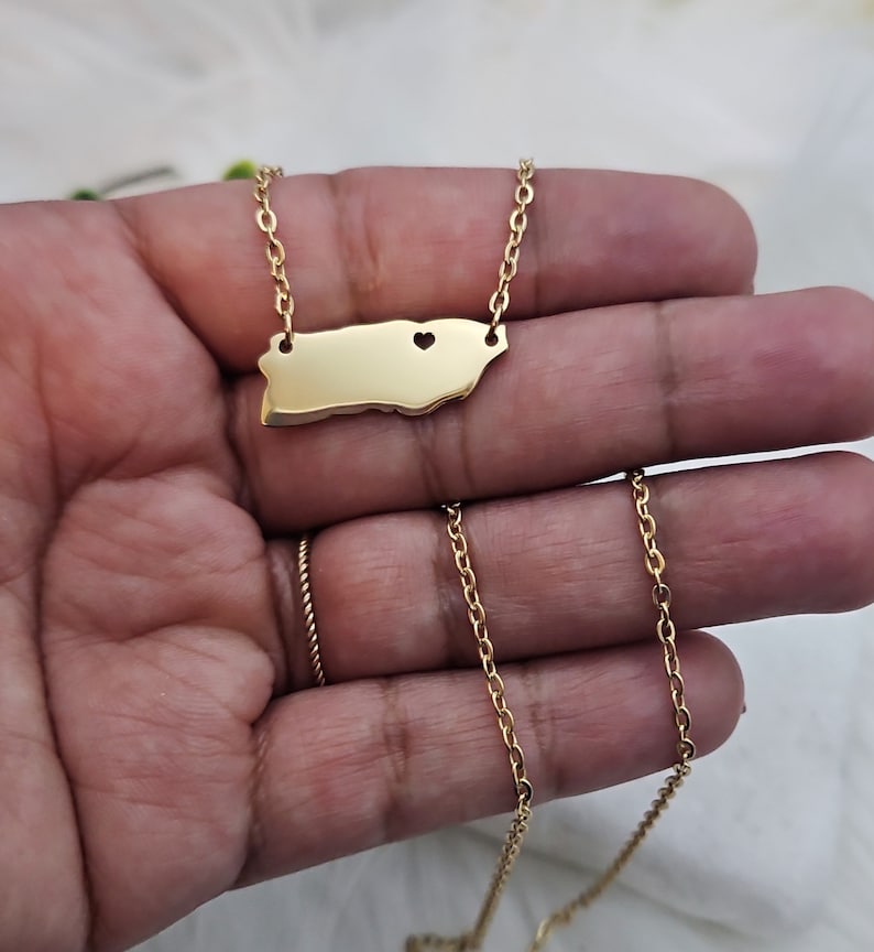 May include: A gold chain necklace with a pendant shaped like the island of Puerto Rico. The pendant has a small heart cut out of it.