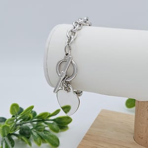 May include: A silver chain bracelet with a toggle clasp and two heart-shaped charms.