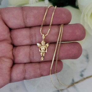 Puede incluir: Un collar de cadena de oro con un peque&ntilde;o colgante de querub&iacute;n. La cadena es de estilo cadena de caja.