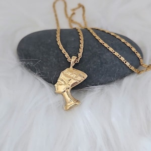 May include: A gold chain necklace with a pendant featuring a profile of an Egyptian queen wearing a headdress.