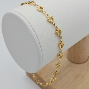 以下が含まれることがあります： 繊細なチェーンとオープンハートのチャームが付いたゴールドトーンのブレスレットです。