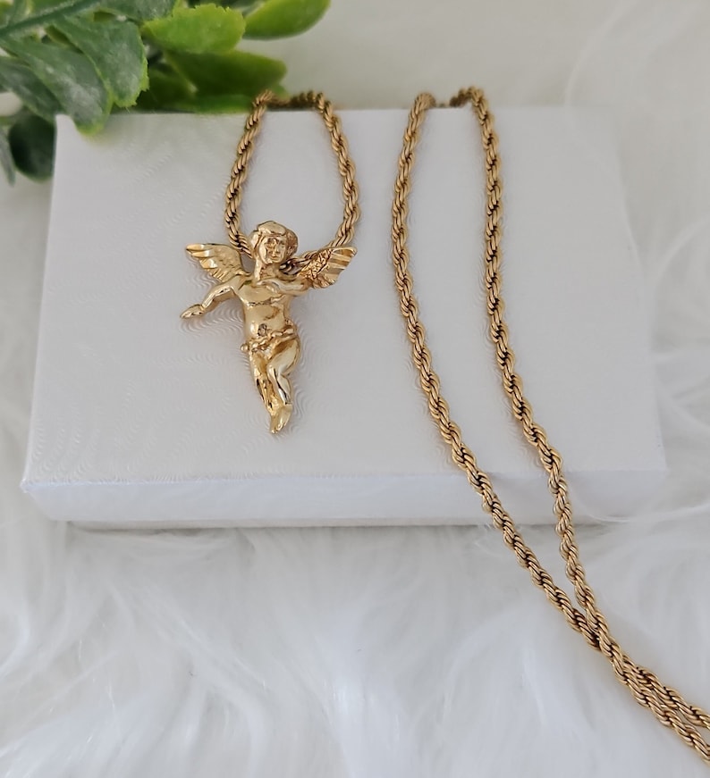 May include: A gold chain necklace with a cherub pendant. The chain is a rope style and the pendant is detailed with wings and a floral design.