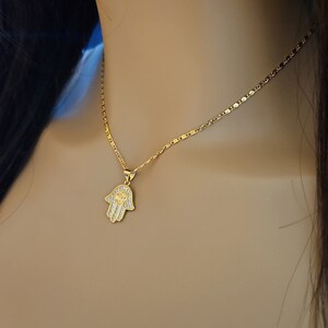 May include: A gold chain necklace with a small hamsa hand pendant encrusted with clear stones.