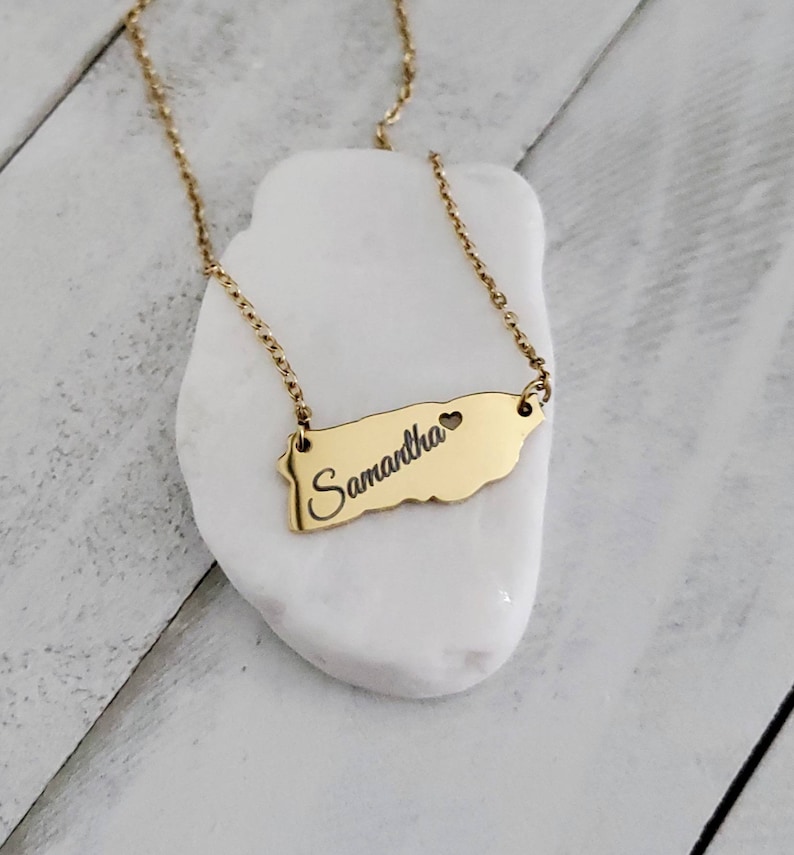 May include: Gold necklace with a pendant shaped like the island of Puerto Rico. The pendant has the name "Samantha" and a small heart engraved on it.