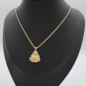 May include: A gold-toned necklace featuring a rope chain and a pendant shaped like a seated, smiling Buddha figure. The pendant has a polished finish and is suspended from a classic twisted metal chain, creating a cohesive gold-colored jewelry piece.