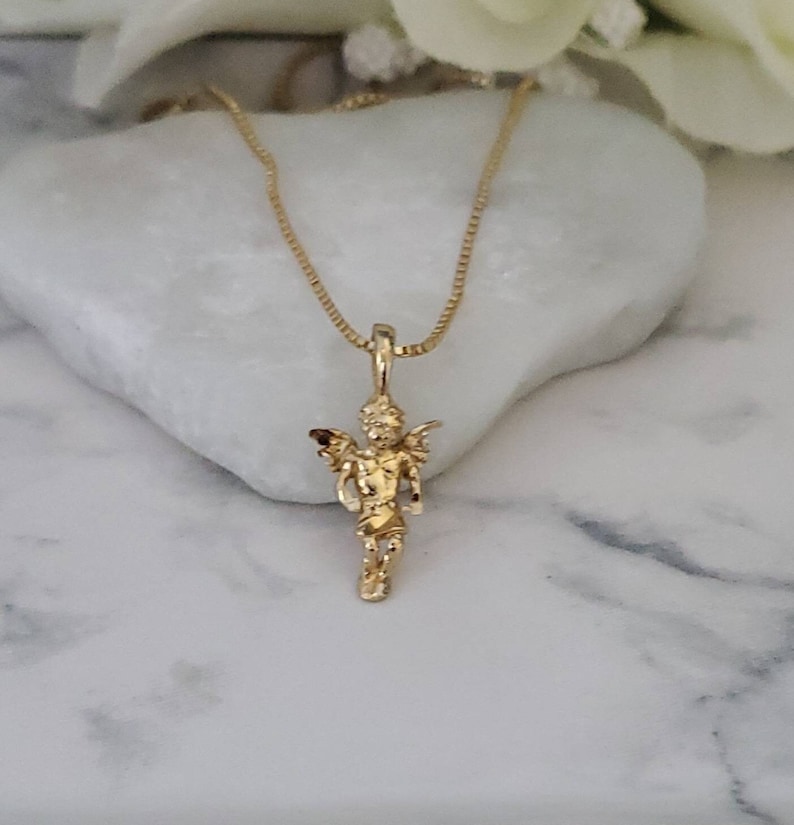 Puede incluir: Un collar de cadena de oro con un peque&ntilde;o colgante de &aacute;ngel. El &aacute;ngel est&aacute; de pie con las alas extendidas y tiene un dise&ntilde;o detallado.