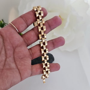 May include: A gold-toned bracelet with a box chain design. The bracelet is made of metal and has a polished finish.