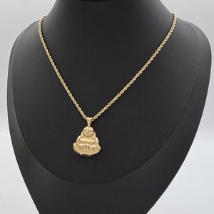 May include: A gold-toned necklace featuring a rope chain and a pendant shaped like a seated, smiling Buddha figure. The pendant has a polished finish and is suspended from a classic twisted metal chain, creating a cohesive gold-colored jewelry piece.