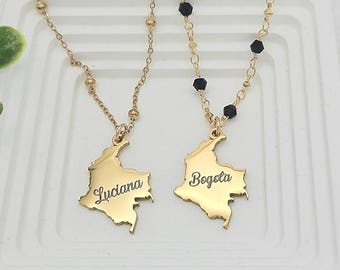 May include: Two gold-colored necklaces with pendants shaped like the country of Colombia. One pendant says "Luciana" and the other says "Bogota". The necklaces have delicate chains with small gold beads and black beads.