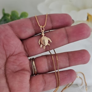 May include: A gold chain necklace with a small, detailed turtle pendant. The chain is box style and the pendant is textured.