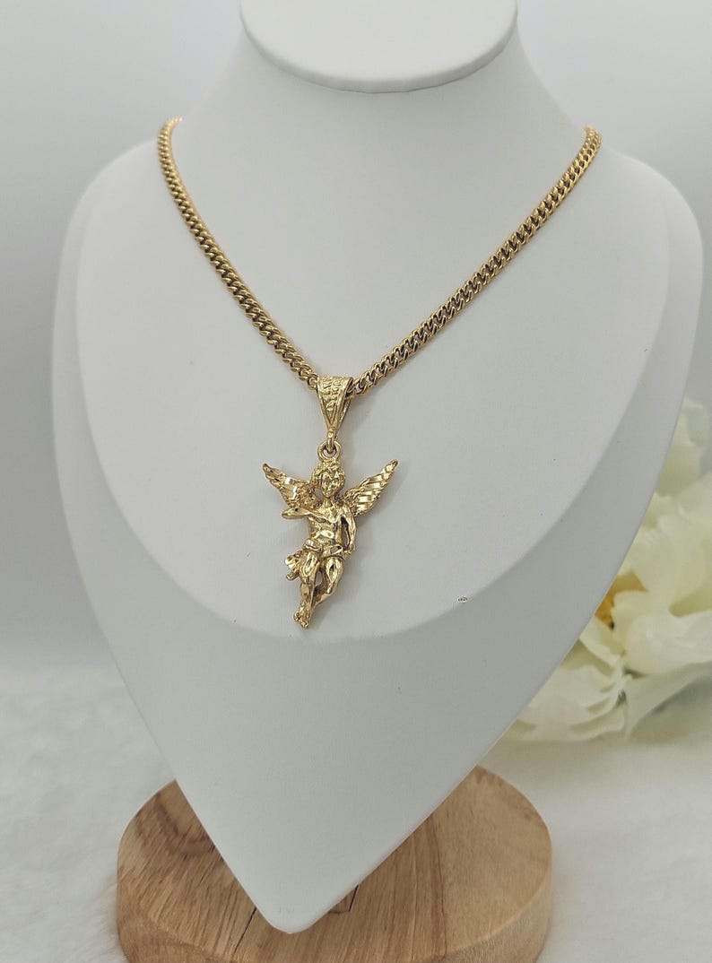 K&ouml;nnte beinhalten: Goldfarbene Halskette mit detailliertem Anh&auml;nger in Form eines Engels mit ausgebreiteten Fl&uuml;geln. Die Kette ist eine Panzerkette. Die Halskette wird auf einer wei&szlig;en B&uuml;ste pr&auml;sentiert, um das Design hervorzuheben.