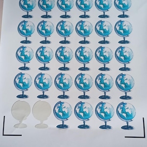 Op de afbeelding: Een vel stickers met een herhalend patroon van blauw-witte wereldbollen in aquarel-stijl op een standaard. Het raster bevat vierendertig stickers, met twee lege cirkelvormige ruimtes waar stickers uit de onderste rij zijn verwijderd.