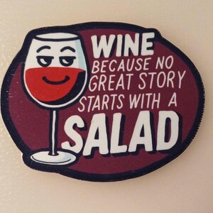 Può includere: Un bicchiere di vino rosso con un viso sorridente su uno sfondo bordeaux con il testo "Wine because no great story starts with a salad".