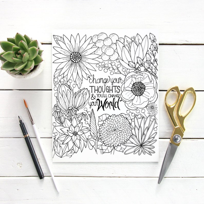 May include: A black and white floral coloring page with the text "change your thoughts & you'll change your world". A succulent in a white pot, a paintbrush, a pen, and gold scissors are on a white wooden surface.