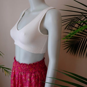 Puede incluir: Top corto blanco de canalé con escote en V. El top se lleva con una falda floral rosa.