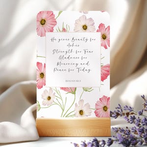 May include: A white card with pink flowers printed on it. The card has a quote about beauty, strength, gladness, mourning, and peace. The quote is from Isaiah 61:3.