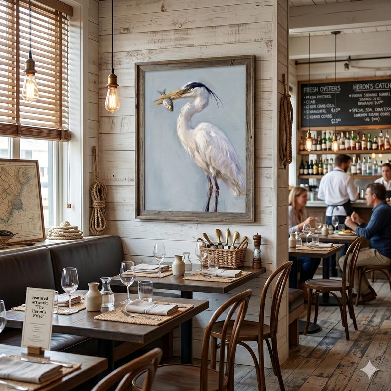 Op de afbeelding: Een ingelijst schilderij van een witte reiger met een vis in zijn bek hangt aan een wit betegelde muur. Het schilderij bevindt zich in een restaurant met tafels, stoelen en een bar op de achtergrond. Het restaurant heeft een nautisch thema.