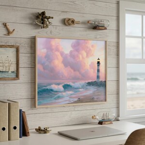 Op de afbeelding: Een ingelijst kustlandschap toont een vuurtoren op een strand met golven onder een roze en paarse lucht. Nautische decoratie omvat een schip in een fles, een touwknoop en een klein messing instrument.