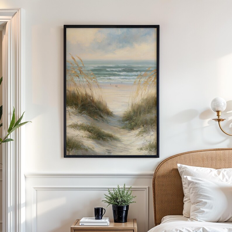 May include: A framed wall art print depicting a coastal landscape with sand dunes, tall beach grass, and a view of the ocean under a soft sky. The painting features muted tones of beige, green, and blue, capturing a serene beach scene.