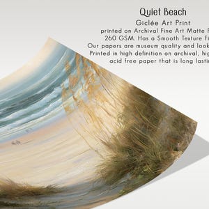 May include: A Gicl&eacute;e art print titled Quiet Beach on archival fine art matte paper with a 260 GSM smooth texture finish. The print features a coastal scene with golden beach grass in the foreground, a sandy shore, and blue ocean waves.
