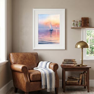 Op de afbeelding: Een ingelijste aquarel van een zeilboot op het water bij zonsondergang. Het kunstwerk toont een witte zeilboot met een enkel zeil, tegen een achtergrond van een kleurrijke lucht met tinten roze, oranje en blauw. De schildering zit in een witte lijst.