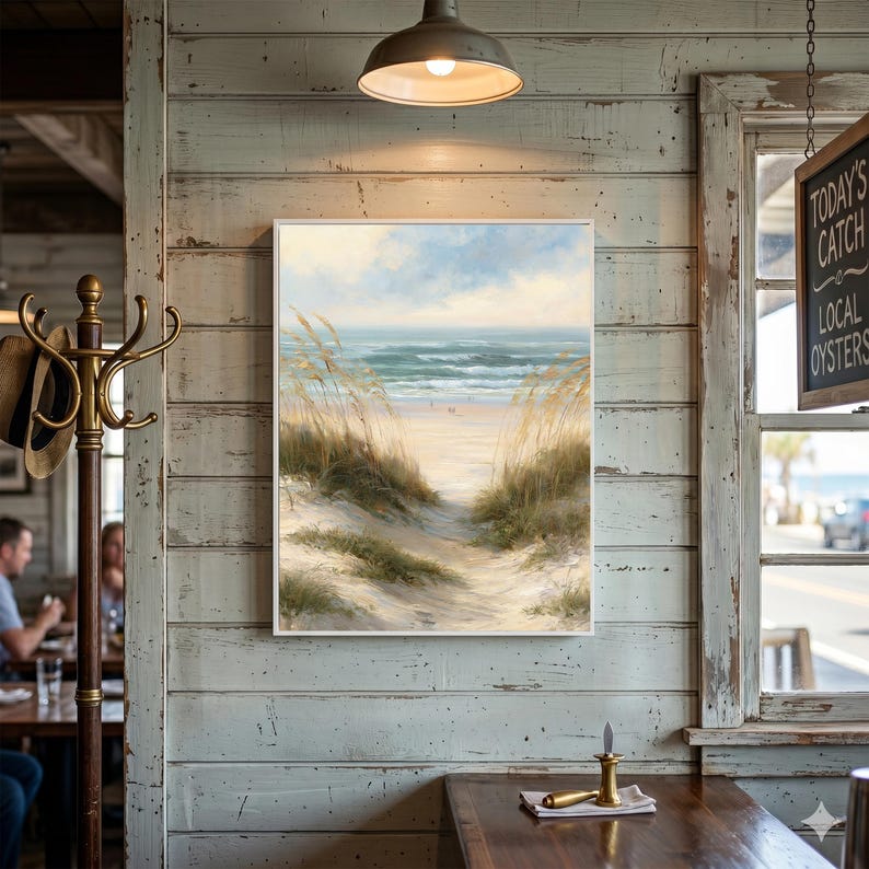 May include: A rectangular wall art print featuring a coastal landscape painting of a sandy beach path lined with tall, golden sea oats leading toward the ocean waves under a soft, light blue sky with scattered clouds, framed in a thin white border.