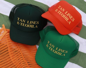 May include: Three green and orange mesh trucker hats with the text "Tan Lines & Tequila" in yellow on a green and white striped beach towel.