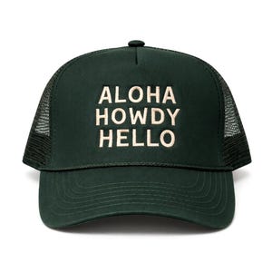 May include: A dark green trucker hat featuring a mesh back and a solid front panel. The text ALOHA HOWDY HELLO is embroidered in a light beige color on the front. The hat includes a matching dark green brim with decorative stitching details.