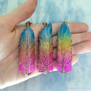 May include: Three rainbow crystal pendants with a copper wire tree design. The crystals are a gradient of pink, orange, yellow, green, and blue.