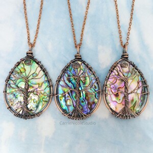 May include: Three copper wire wrapped pendants featuring a tree of life design with abalone shell inlay. The pendants are on copper chains.
