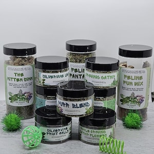 May include: A variety of catnip and silvervine blends in clear glass jars with black lids. The jars are labeled with the names of the blends, such as "The Kitten Dink", "Feline Fun Mix", and "Silvervine Leaf". There are also two green cat toys in the image.