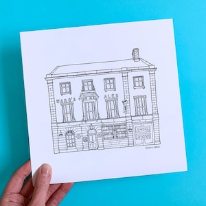 May include: Black and white line drawing of a pub with the text "Ward's Fine Bay Ales". The building has multiple windows and a chimney. The artwork is held by a hand against a bright blue background.