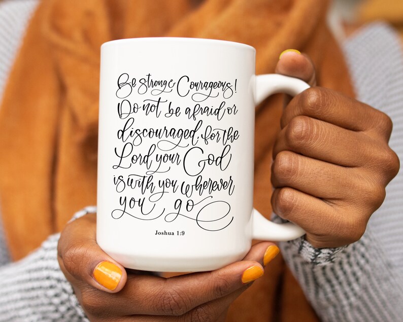 May include: White ceramic mug with a large handle, featuring the scriptural quote "Be Strong & Courageous! Do not be afraid or discouraged for the Lord your God is with you wherever you go" from Joshua 1:9 in black script.