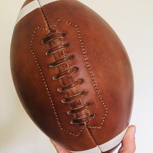 May include: A brown leather football with white stripes. The football is stitched with brown leather thread.