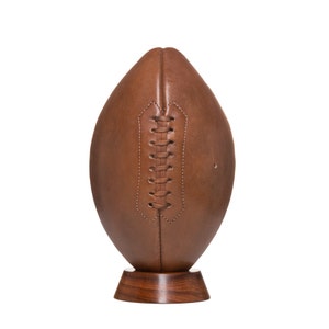 May include: A brown leather football on a wooden stand. The football has laces and is displayed on a dark brown wooden base.