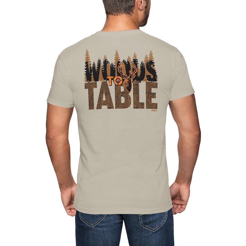 May include: A beige t-shirt with a black and orange graphic print that says "Woods to Table" with a silhouette of a deer in the middle of the word "Woods".