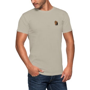 May include: A light beige t-shirt with a small brown bear graphic on the left chest.