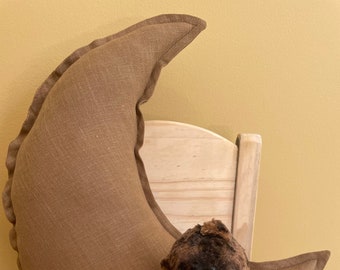 May include: A brown teddy bear with a pink polka dot bow sits on a wooden chair with a brown crescent moon pillow behind it.