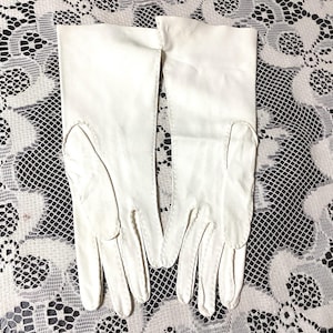 May include: A pair of white leather gloves with a long cuff. The gloves are made of a smooth, soft leather and have a classic design.