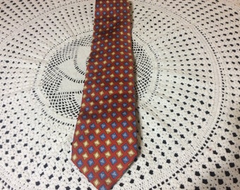May include: A red, blue, and yellow patterned tie with a geometric design. The tie is made of silk and has a pointed tip.