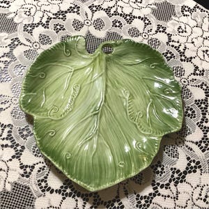 May include: A green ceramic leaf-shaped serving dish with a raised design. The dish is perfect for serving snacks or appetizers.
