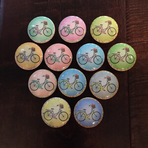 May include: Twelve colorful round ceramic knobs with a bicycle design. Each knob features a different color background and a bicycle with a basket.