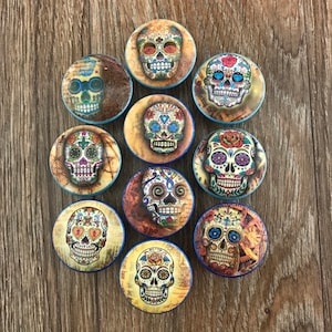 May include: A collection of eleven round, colorful Day of the Dead skull magnets. Each magnet features a unique sugar skull design with intricate patterns and vibrant colors, set against a vintage-style background.