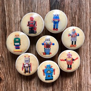 May include: Set of eight ceramic knobs featuring vintage robot illustrations. Each knob has a different robot design with various colors, including red, blue, green, and silver. The knobs are perfect for adding a whimsical touch to furniture.