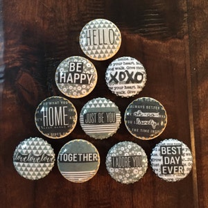 May include: Nine round gray and white patterned magnets with yellow trim. Each magnet has a different inspirational quote. The quotes are: "Hello", "Be Happy", "XOXO", "Do What You Love Home", "Just Be You", "Always Better When Oh-So Lonely", "Love Love Love", "Together", "I Adore You", and "Best Day Ever".