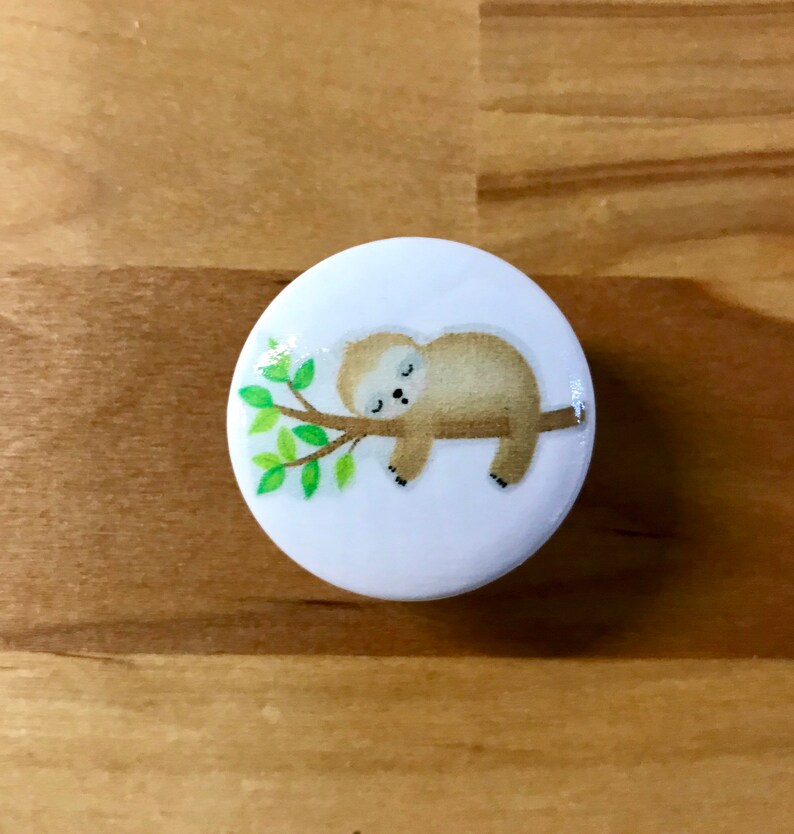 May include: A white ceramic knob with a cartoon image of a brown sloth sleeping on a green branch.